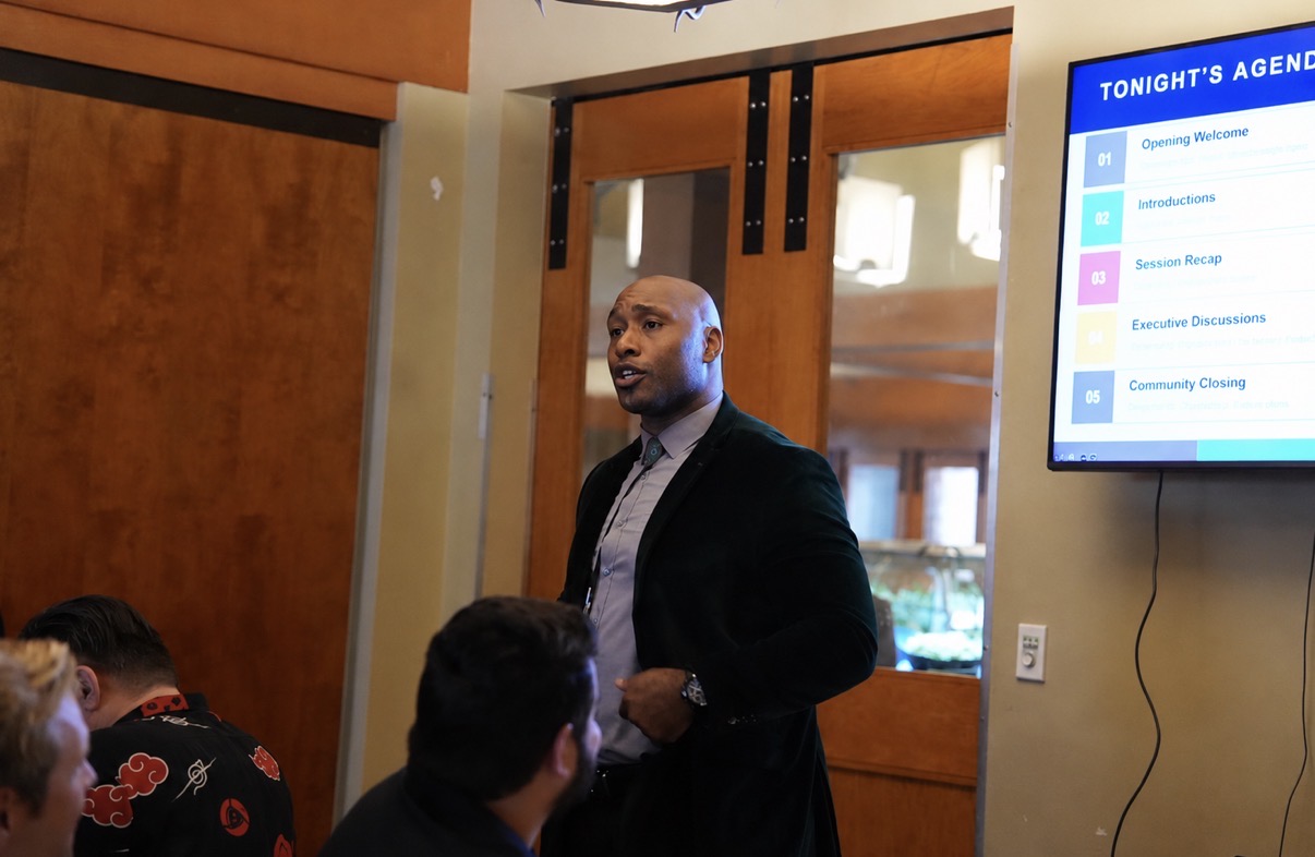 Speaker presenting beside the evening agenda at a Cyber In Color event